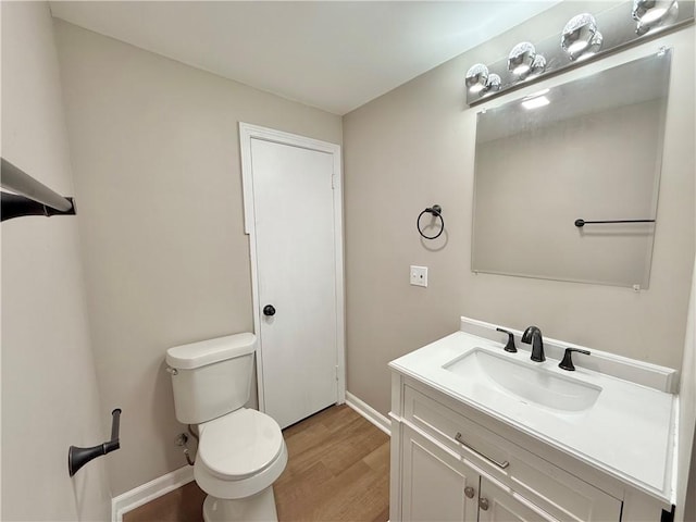 half bath with vanity, wood finished floors, toilet, and baseboards