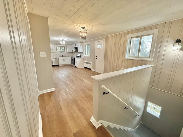 corridor with light wood-style flooring, radiator heating unit, a sink, an upstairs landing, and wooden ceiling