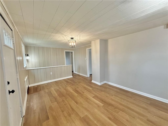 unfurnished room featuring light wood-type flooring, an inviting chandelier, and baseboards