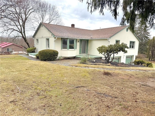 view of front facade with a shingled roof, a front yard, and a chimney