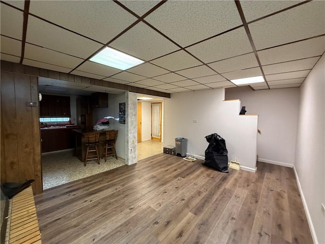 finished basement with baseboards, a drop ceiling, and wood finished floors