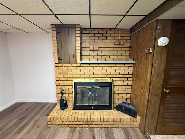 details with a drop ceiling, a brick fireplace, wood finished floors, and baseboards