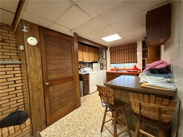 kitchen with a paneled ceiling, a sink, light floors, and separate washer and dryer