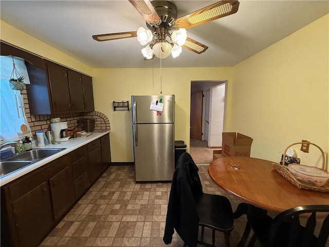 kitchen featuring dark brown cabinetry, light countertops, backsplash, and freestanding refrigerator