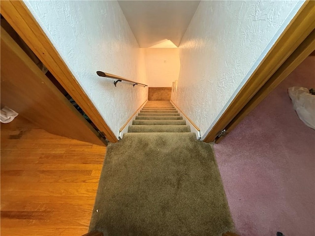 staircase featuring a textured wall, carpet flooring, and baseboards