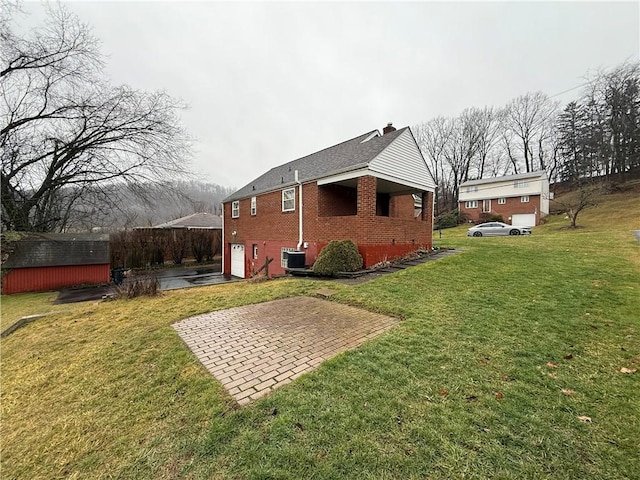 view of property exterior with brick siding, a yard, a chimney, central air condition unit, and a garage