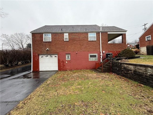 exterior space featuring aphalt driveway, an attached garage, a yard, central AC, and brick siding