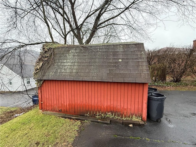 view of side of home featuring a storage shed, a shingled roof, and an outdoor structure