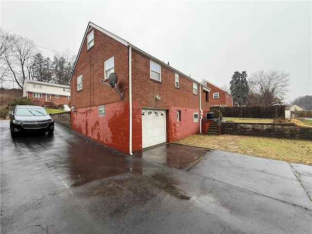 view of property exterior featuring driveway, an attached garage, fence, and brick siding