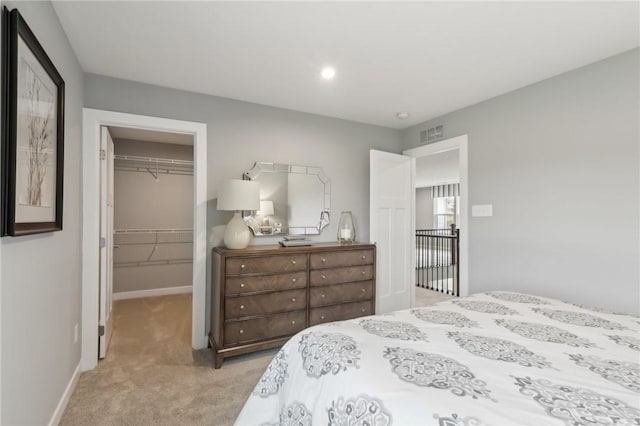 bedroom with baseboards, visible vents, light colored carpet, a walk in closet, and a closet