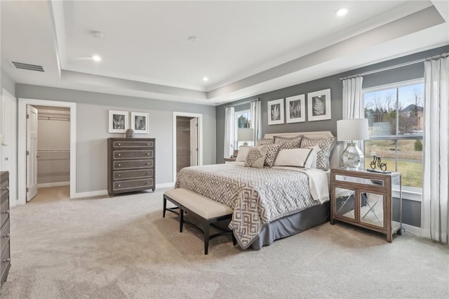 bedroom with a tray ceiling, light colored carpet, visible vents, a spacious closet, and baseboards