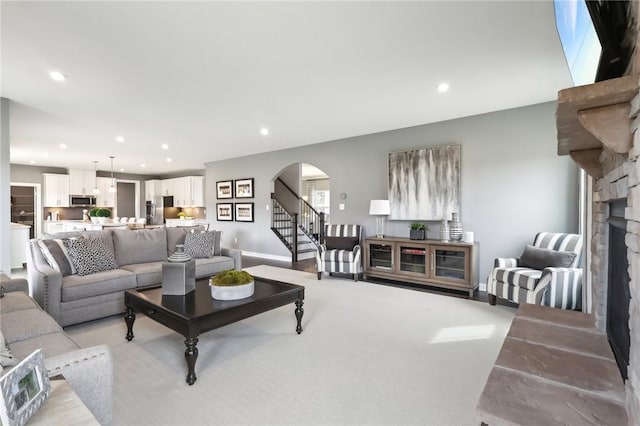 living area with arched walkways, a stone fireplace, recessed lighting, baseboards, and stairway