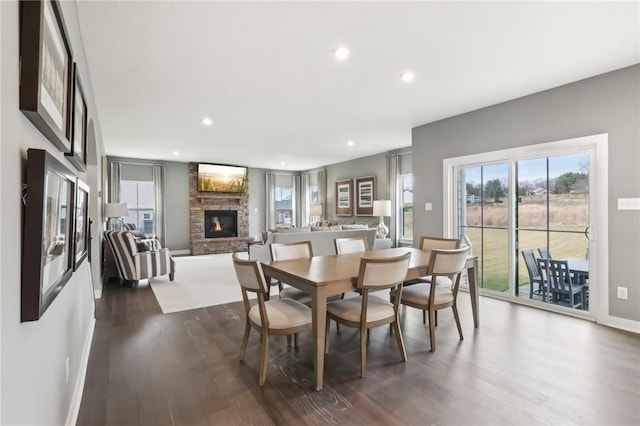 dining room featuring baseboards, a stone fireplace, dark wood-style flooring, and recessed lighting