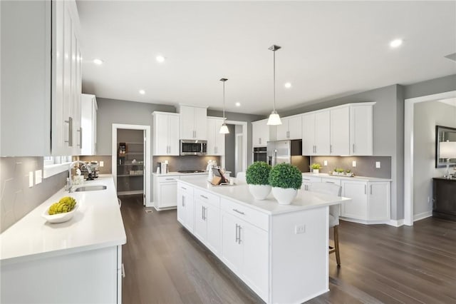 kitchen with stainless steel appliances, a sink, white cabinetry, backsplash, and a center island