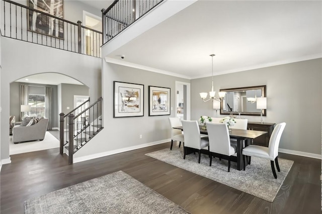 dining space featuring a notable chandelier, wood finished floors, a towering ceiling, baseboards, and stairway