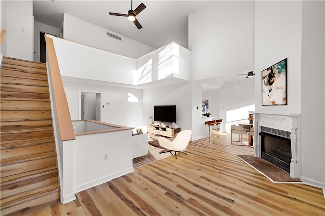 living area with visible vents, a ceiling fan, light wood-style flooring, stairs, and a fireplace