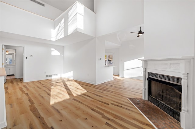 unfurnished living room with a towering ceiling, a multi sided fireplace, visible vents, and light wood-style floors