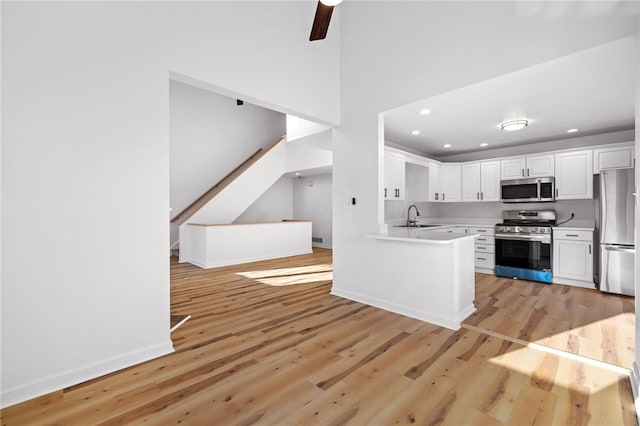 kitchen with light wood-style flooring, appliances with stainless steel finishes, light countertops, white cabinetry, and a sink