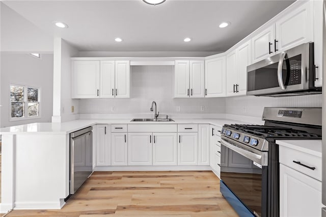 kitchen featuring a peninsula, appliances with stainless steel finishes, a sink, and white cabinetry