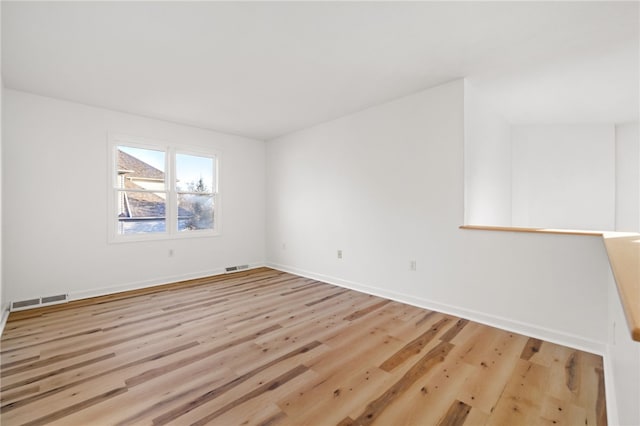 spare room with wood finished floors, visible vents, and baseboards