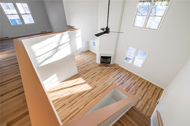 interior space with a fireplace, visible vents, a towering ceiling, ceiling fan, and wood finished floors