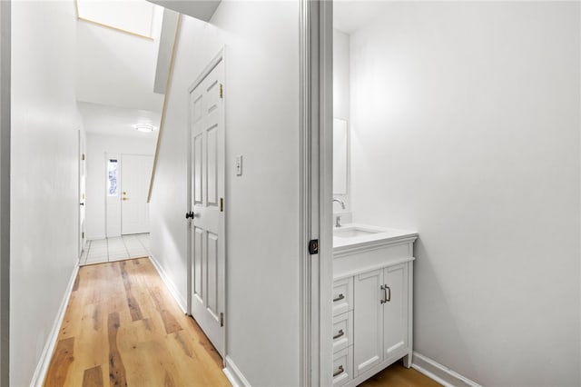 hall featuring light wood-style floors, baseboards, and a sink