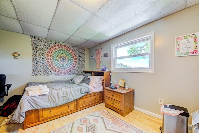 bedroom featuring light wood-style floors, a drop ceiling, and baseboards