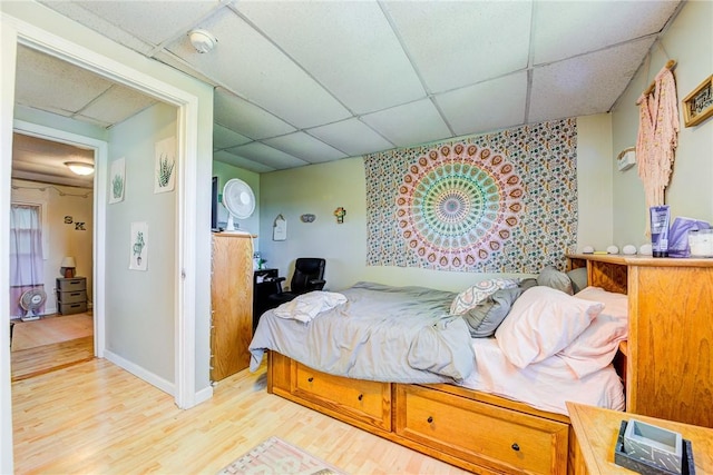 bedroom with light wood-type flooring, a paneled ceiling, and baseboards