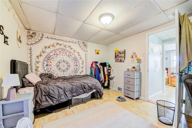 bedroom featuring a drop ceiling, wood finished floors, visible vents, and baseboards