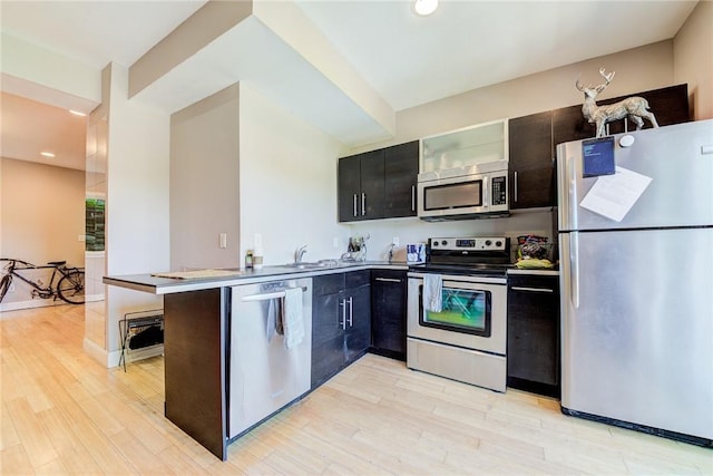 kitchen with stainless steel appliances, a peninsula, a sink, light wood-type flooring, and glass insert cabinets