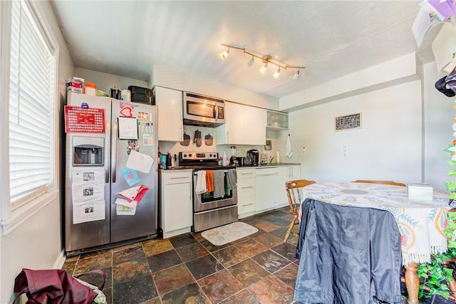 kitchen with stone finish flooring, appliances with stainless steel finishes, dark countertops, and white cabinets