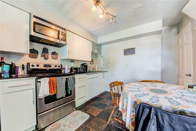 kitchen featuring appliances with stainless steel finishes, stone finish floor, dark countertops, and white cabinets