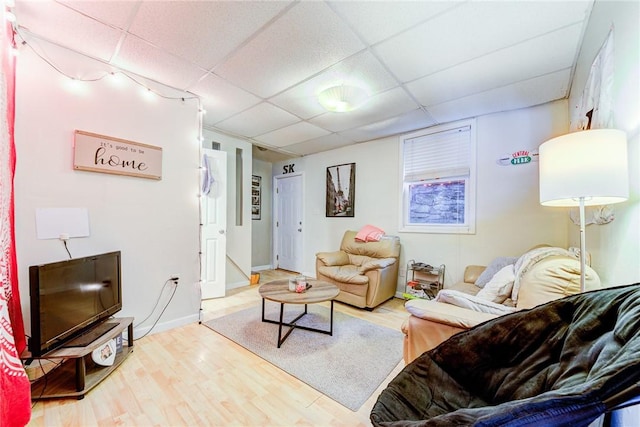 living room featuring a paneled ceiling, baseboards, and wood finished floors