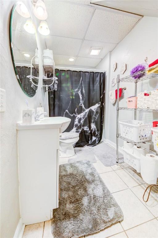 full bathroom with baseboards, a drop ceiling, toilet, tile patterned floors, and vanity