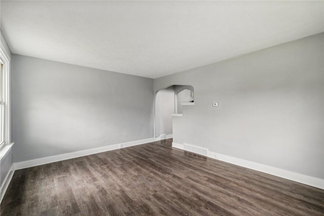spare room with arched walkways, visible vents, dark wood-type flooring, and baseboards