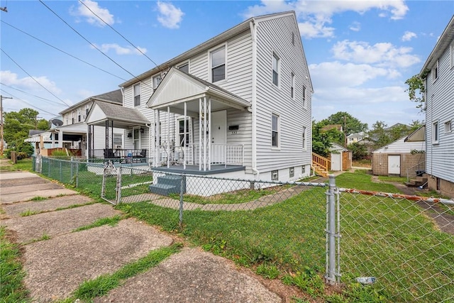view of front of house with a front yard, an outbuilding, covered porch, a fenced front yard, and a storage shed