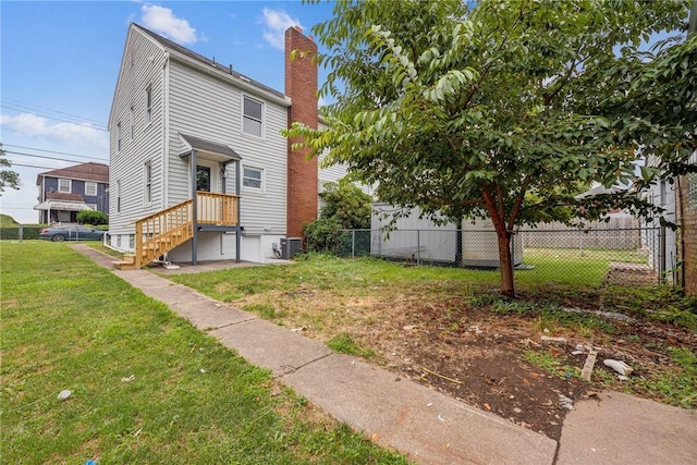 rear view of house featuring central air condition unit, a lawn, fence, and a chimney