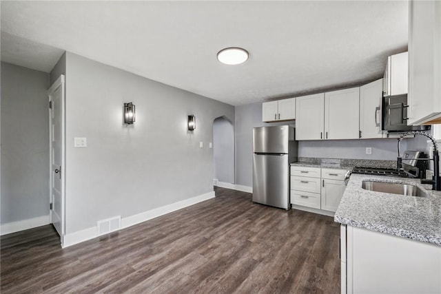 kitchen featuring light stone countertops, visible vents, arched walkways, freestanding refrigerator, and white cabinets