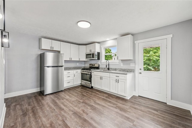 kitchen with light stone counters, wood finished floors, a sink, white cabinets, and appliances with stainless steel finishes