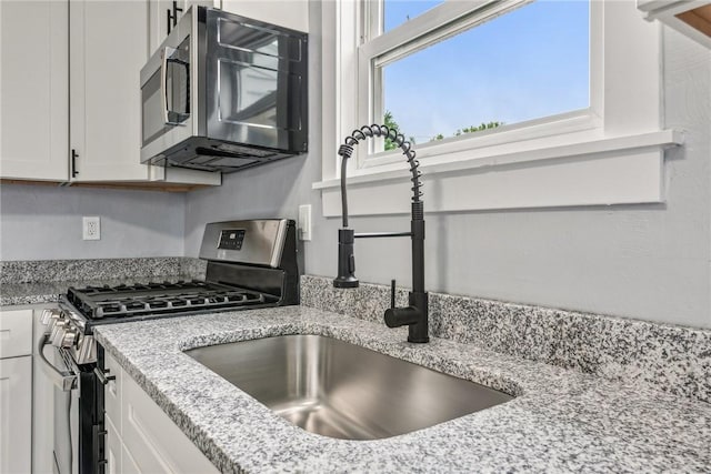 kitchen featuring light stone counters, white cabinets, appliances with stainless steel finishes, and a sink