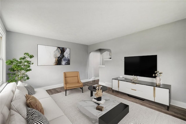 living area with wood finished floors, arched walkways, and baseboards