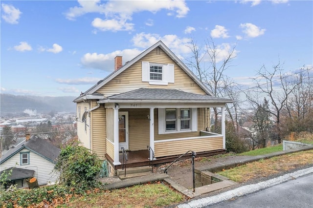 bungalow-style house with a shingled roof, a chimney, and a porch