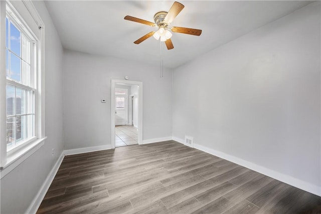 empty room with wood finished floors, a ceiling fan, and baseboards