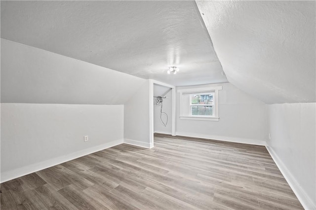 bonus room with a textured ceiling, vaulted ceiling, wood finished floors, and baseboards