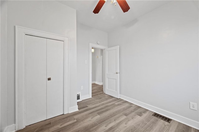 unfurnished bedroom featuring a closet, visible vents, a ceiling fan, wood finished floors, and baseboards