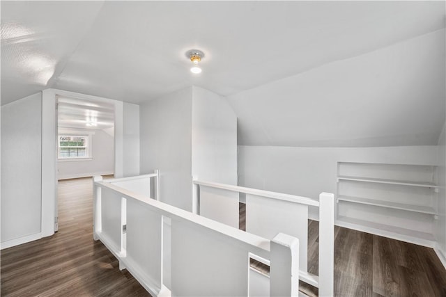 hall featuring built in shelves, vaulted ceiling, wood finished floors, and an upstairs landing