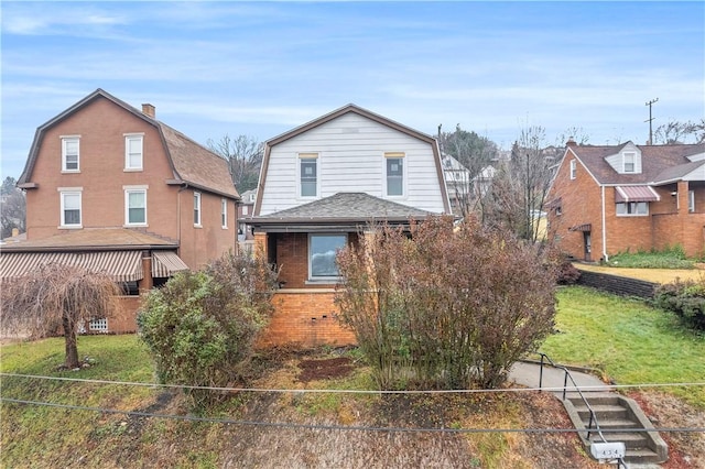 view of front of house with roof with shingles, brick siding, a front lawn, and a gambrel roof