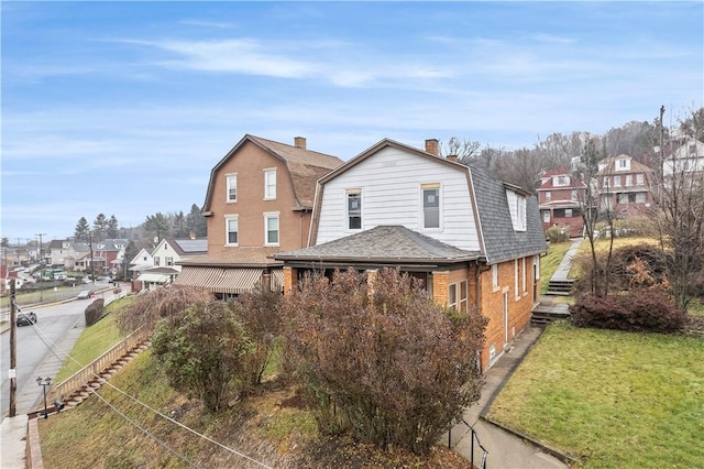 view of front facade featuring a shingled roof, a gambrel roof, a residential view, a front lawn, and brick siding