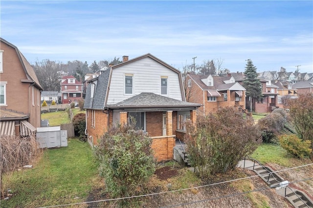 view of front of house with brick siding, a gambrel roof, a residential view, a chimney, and a front yard