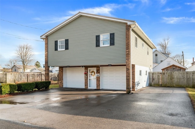 view of side of home with aphalt driveway, brick siding, fence, and an attached garage